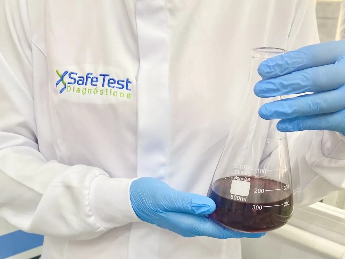 Profissional de jaleco com o logo da SafeTest Diagnósticos segurando um frasco de laboratório